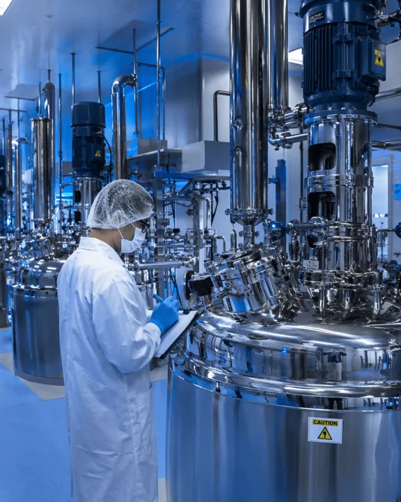 Technician inspecting stainless-steel API reactors in a pharmaceutical cleanroom